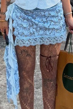 A person wearing a light blue floral lace mini skirt, sheer brown lace tights, and black platform loafers