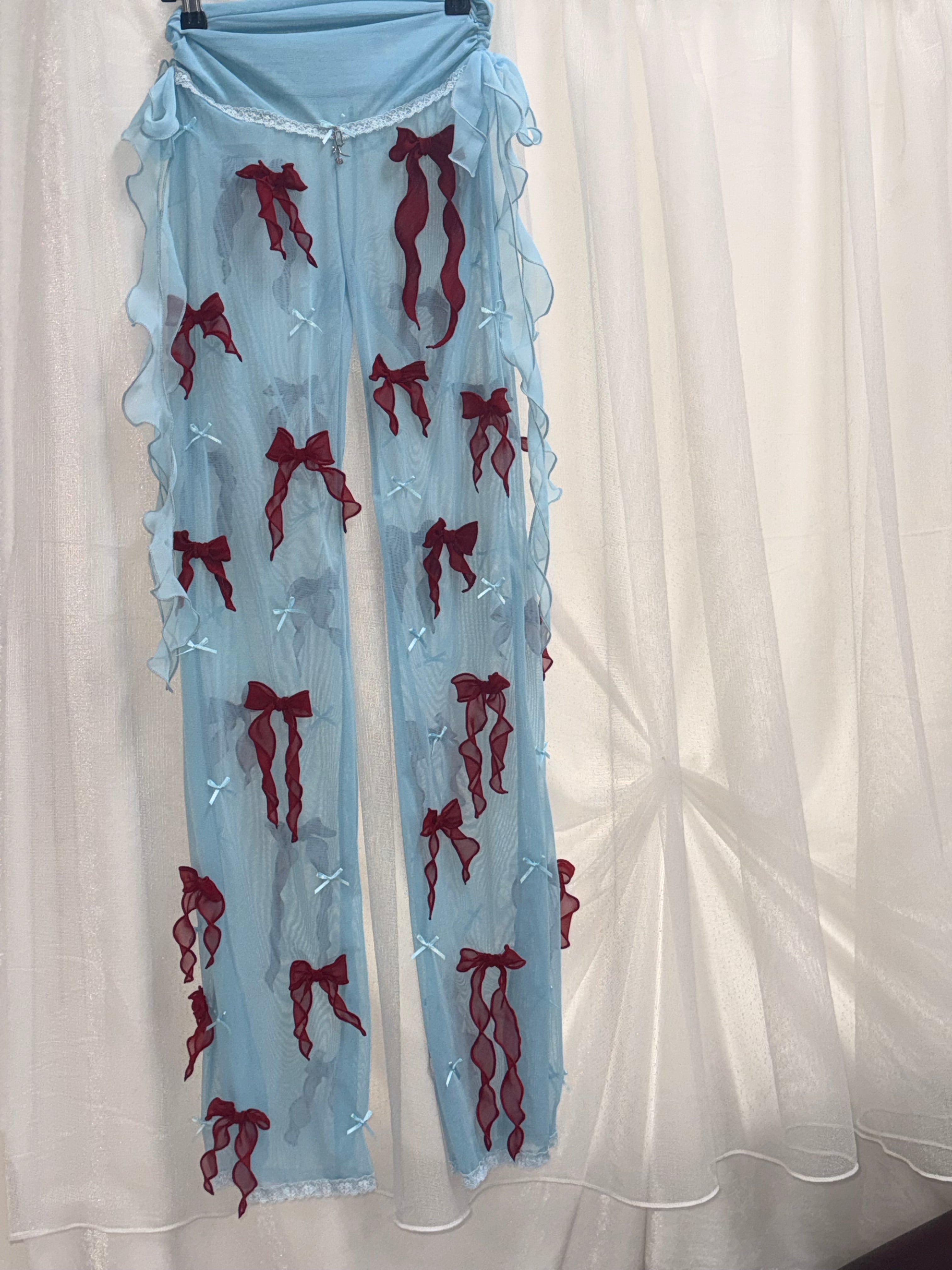 A pair of sheer light blue tights or stockings with embroidered dark red fish motifs and small white cross accents, laid flat on a white fabric background.