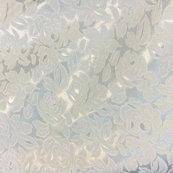 A close-up of a light blue and white floral jacquard fabric with a textured rose pattern, draped over a white surface.
