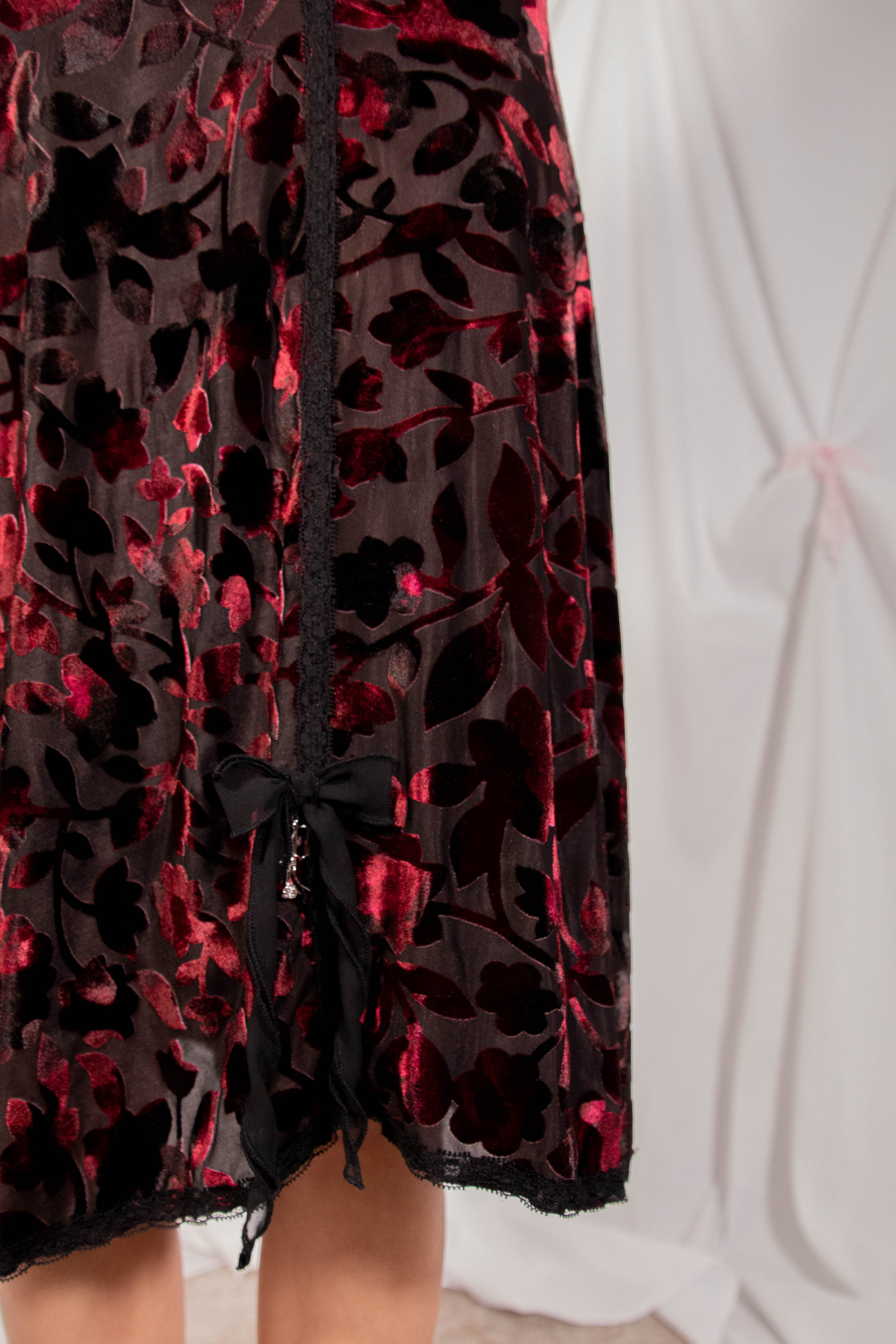 Close-up of a sheer black mesh skirt with a red and black floral velvet pattern, featuring a side tie closure and black lace trim.